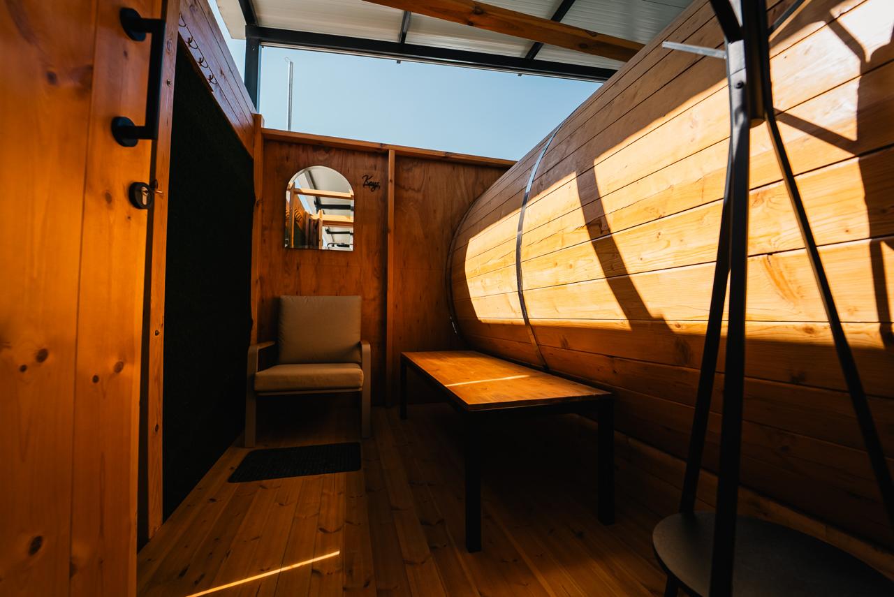 Sunlit wooden lounge beside the barrel sauna with an armchair and table